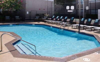 Sonesta ES Suites Dallas Medical Market Center’s outdoor pool has sun loungers as well as armchairs and coffee tables by its side.