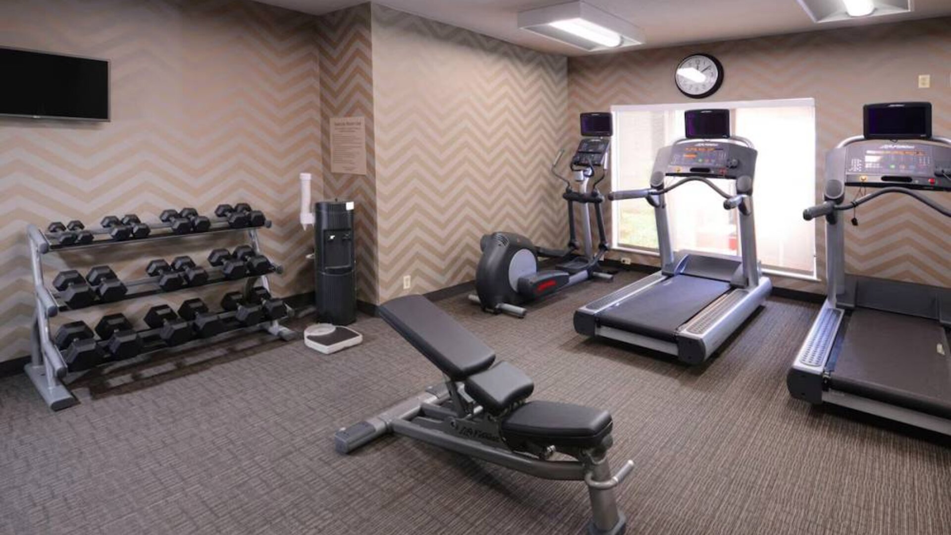 Sonesta ES Suites Dallas Medical Market Center’s fitness center has an assortment of exercise equipment including free weights, and a wall-mounted television.