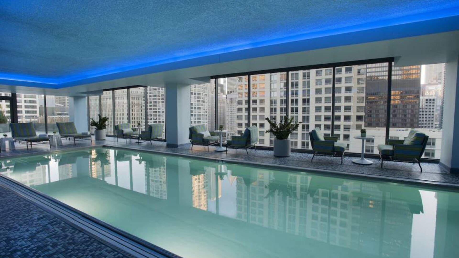 Royal Sonesta Chicago River North’s indoor pool features floor-to-ceiling windows and tables and chairs, and loungers, by the side.