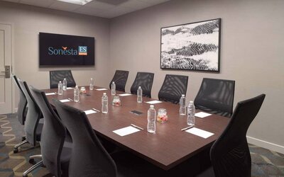 Hotel meeting room including long wooden table, 10 chairs, and a TV and art on the walls.