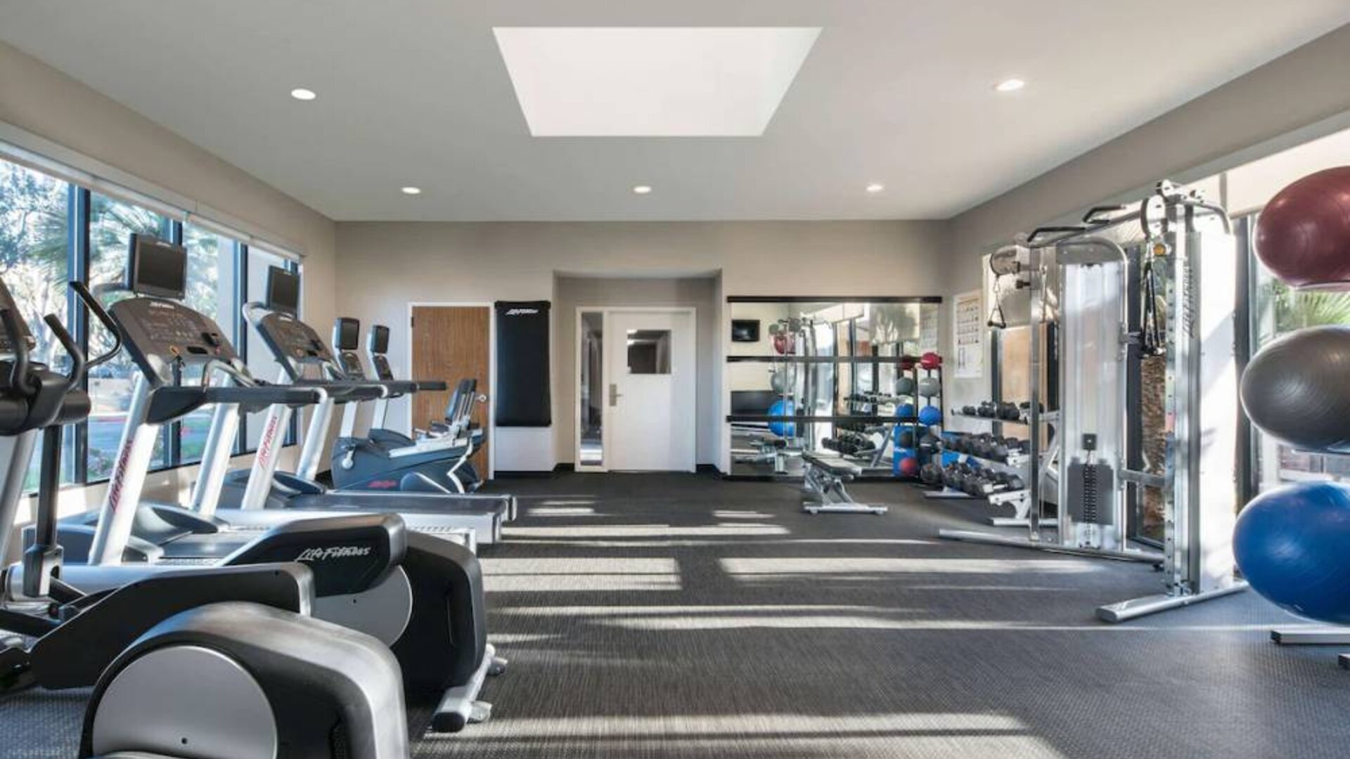 Fitness center equipped with free weights, gym balls, a TV, and various exercise machines at Sonesta Select Los Angeles LAX El Segundo.
