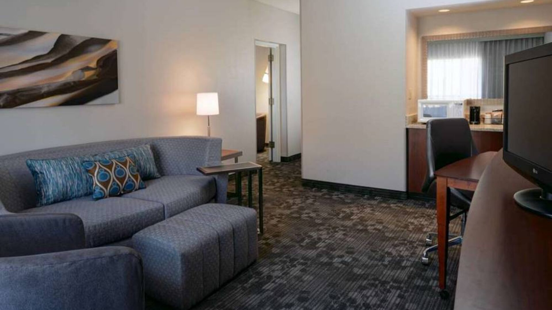 Guest room living area with sofa, chair, and TV at Sonesta Select Kansas City South Overland Park.