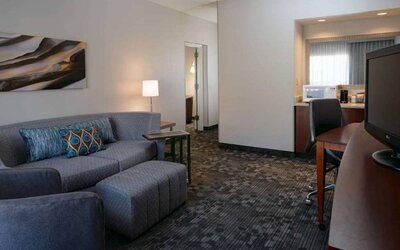 Guest room living area with sofa, chair, and TV at Sonesta Select Kansas City South Overland Park.