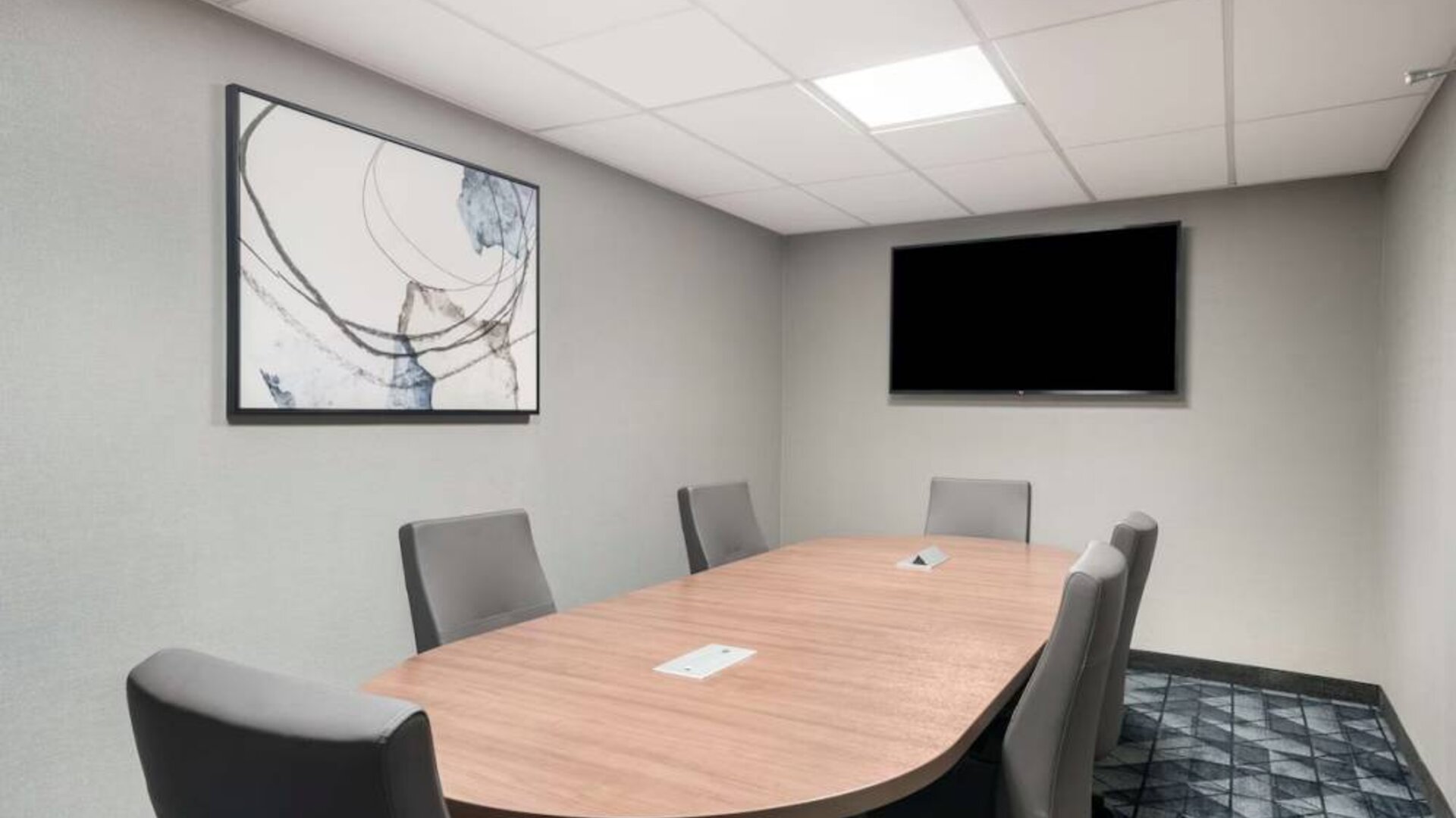 Hotel meeting room with wooden table, half a dozen chairs, and a wall-mounted television.