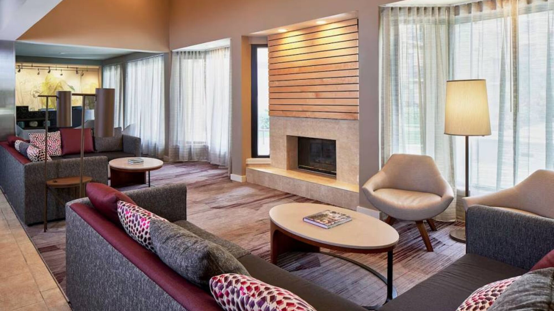 Lounge in the hotel lobby, including large windows, coffee tables, comfy seating, and a fireplace.