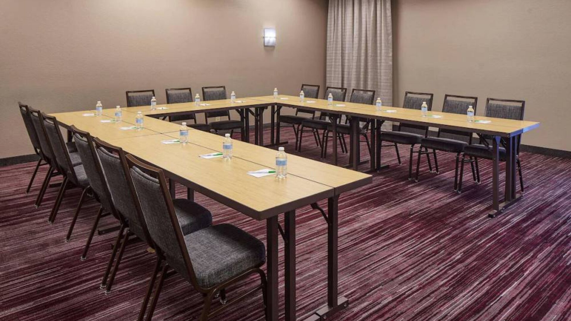 Hotel meeting room with tables arranged in a U-shape and seating for over a dozen attendees.