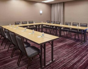 Hotel meeting room with tables arranged in a U-shape and seating for over a dozen attendees.