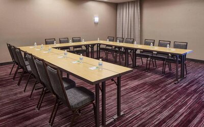 Hotel meeting room with tables arranged in a U-shape and seating for over a dozen attendees.