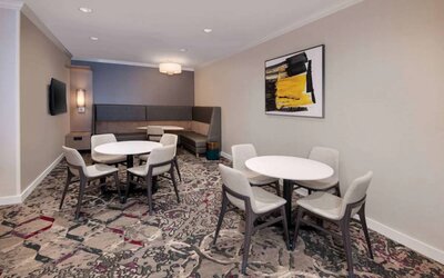 Lobby lounge in Sonesta ES Suites Atlanta Alpharetta North Point Mall with small tables and both art and a large TV on the wall.