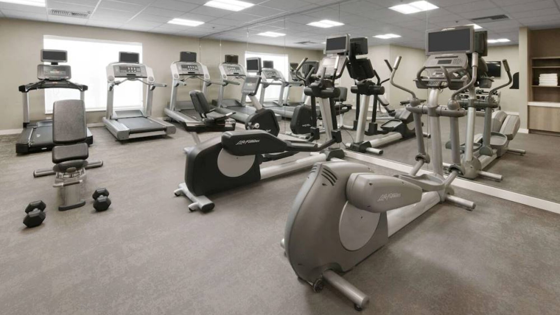 Fitness center at Sonesta ES Suites Fort Worth Fossil Creek, featuring free weights, a mirrored wall, and range of exercise machines.