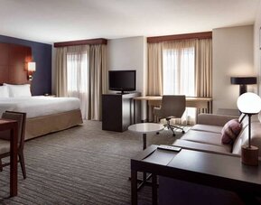 Double bed guest room living area in Sonesta ES Suites Tempe, furnished with sofa, coffee table, chair, desk, and TV.