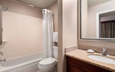 Sonesta ES Suites Tempe guest bathroom, fitted with shower-equipped bath, lavatory, mirror, and sink.