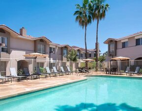 Outdoor pool at Sonesta ES Suites Tempe, featuring shaded tables and chairs, plus sun loungers, by the side.