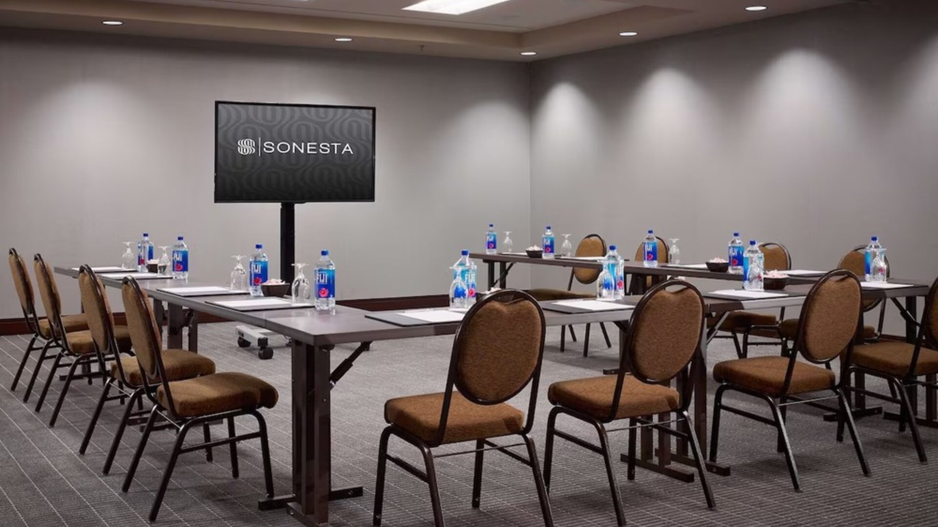 Hotel meeting room, with large table, seating for around 10 attendees, and a large widescreen television.