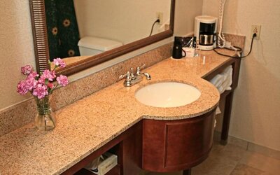 Guest bathroom featuring a granite vanity, large framed mirror, fresh towels, and convenient in-room amenities at Sturbridge Host Hotel.