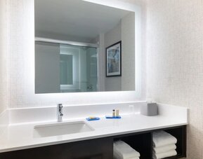 Modern guest bathroom featuring a spacious vanity, illuminated mirror, premium toiletries, and fresh towels at Holiday Inn Express & Suites Boston-Cambridge.