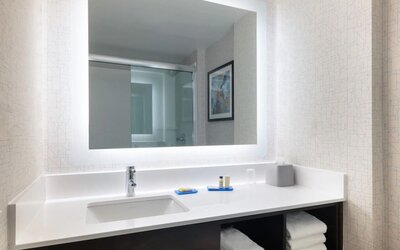 Modern guest bathroom featuring a spacious vanity, illuminated mirror, premium toiletries, and fresh towels at Holiday Inn Express & Suites Boston-Cambridge.