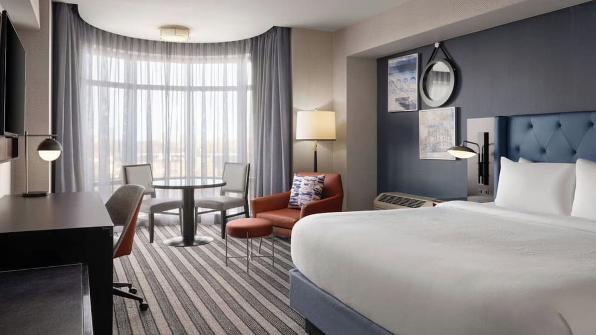 Contemporary king guest room featuring plush bedding, comfortable seating, a dedicated workspace, and large windows that fill the space with natural light at Courtyard by Marriott Boston Brookline.