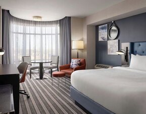 Contemporary king guest room featuring plush bedding, comfortable seating, a dedicated workspace, and large windows that fill the space with natural light at Courtyard by Marriott Boston Brookline.
