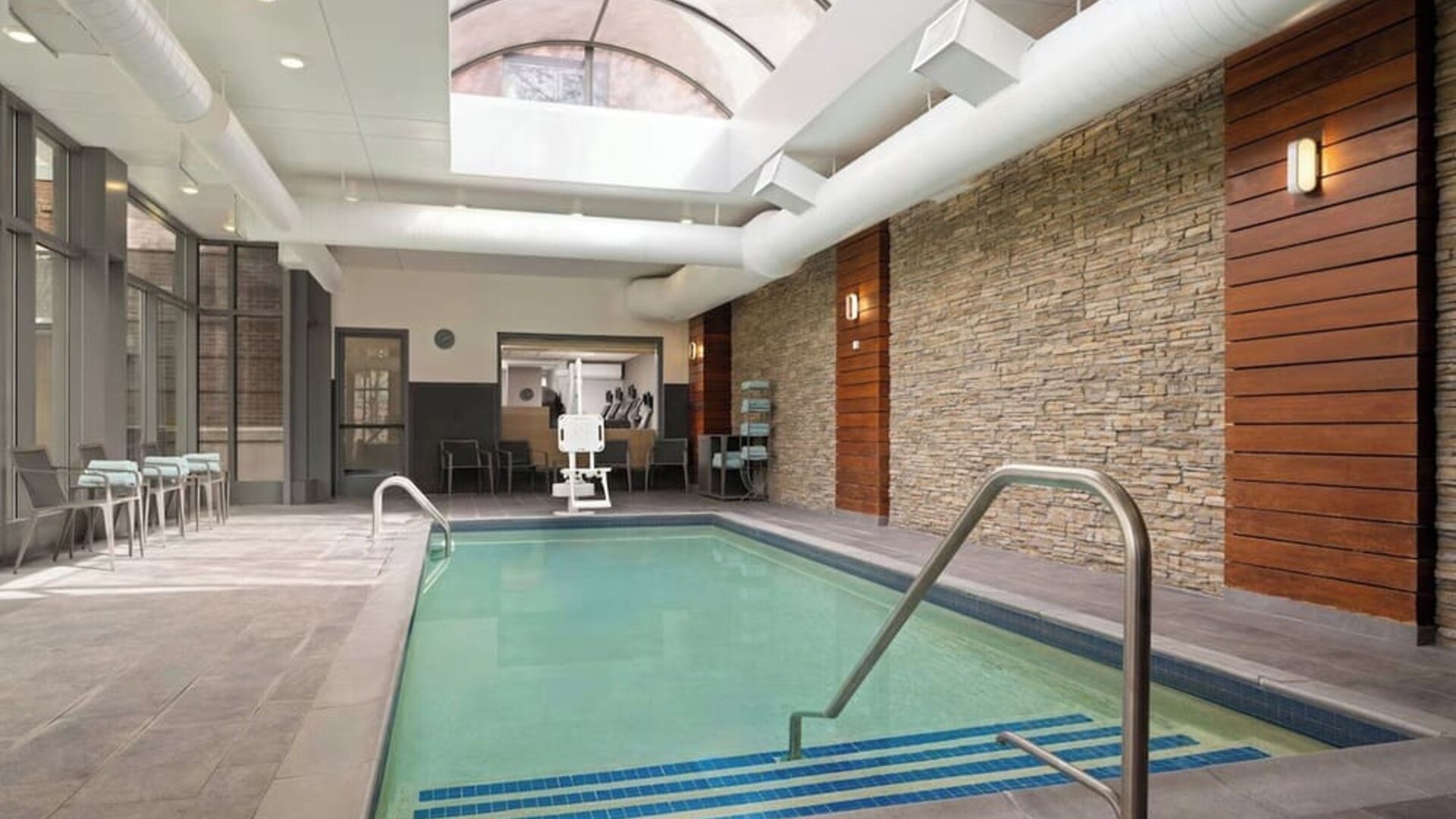 Indoor swimming pool featuring a bright, modern design and comfortable lounge seating for year-round relaxation at Courtyard by Marriott Boston Brookline.