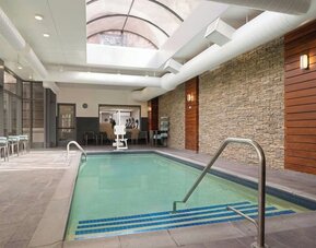 Indoor swimming pool featuring a bright, modern design and comfortable lounge seating for year-round relaxation at Courtyard by Marriott Boston Brookline.