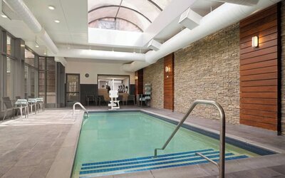 Indoor swimming pool featuring a bright, modern design and comfortable lounge seating for year-round relaxation at Courtyard by Marriott Boston Brookline.