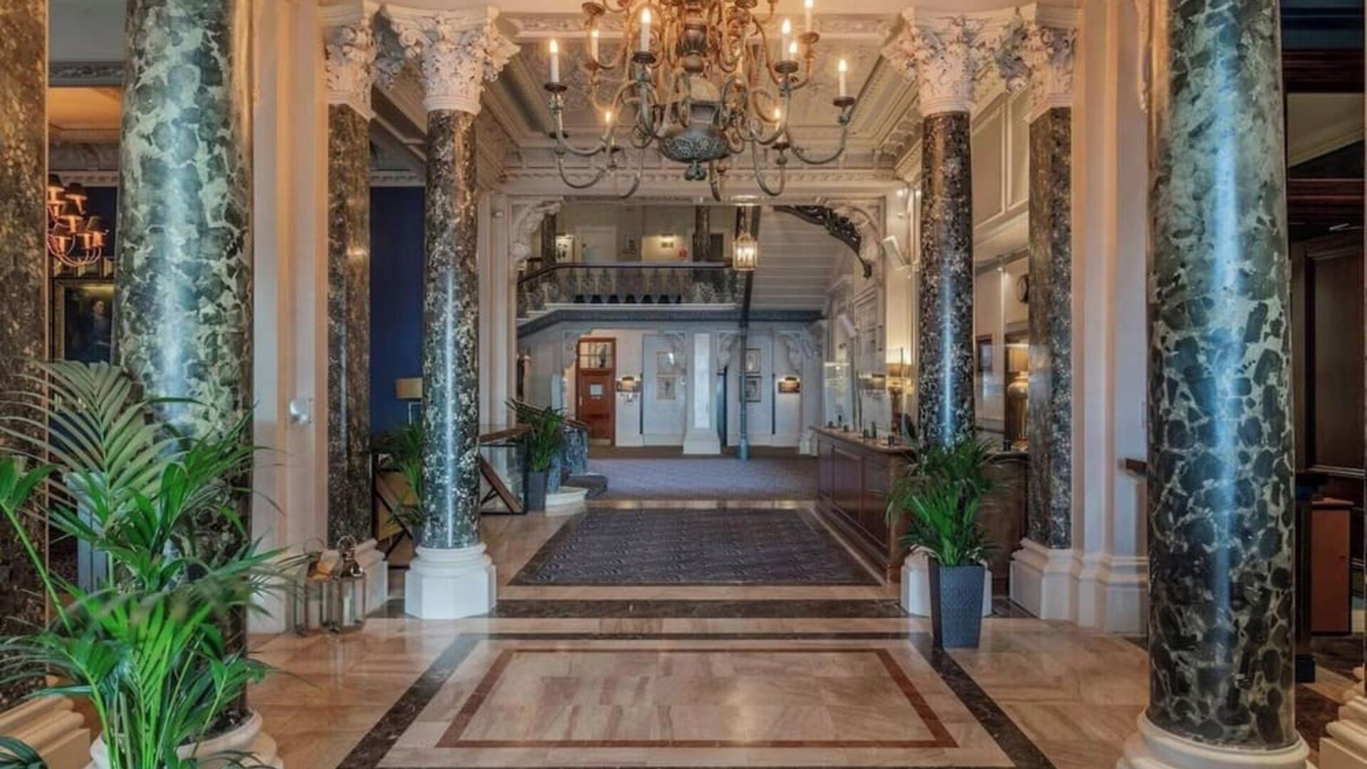 Elegant hotel lobby with marble columns and decorative chandeliers at The Grand Brighton. 
