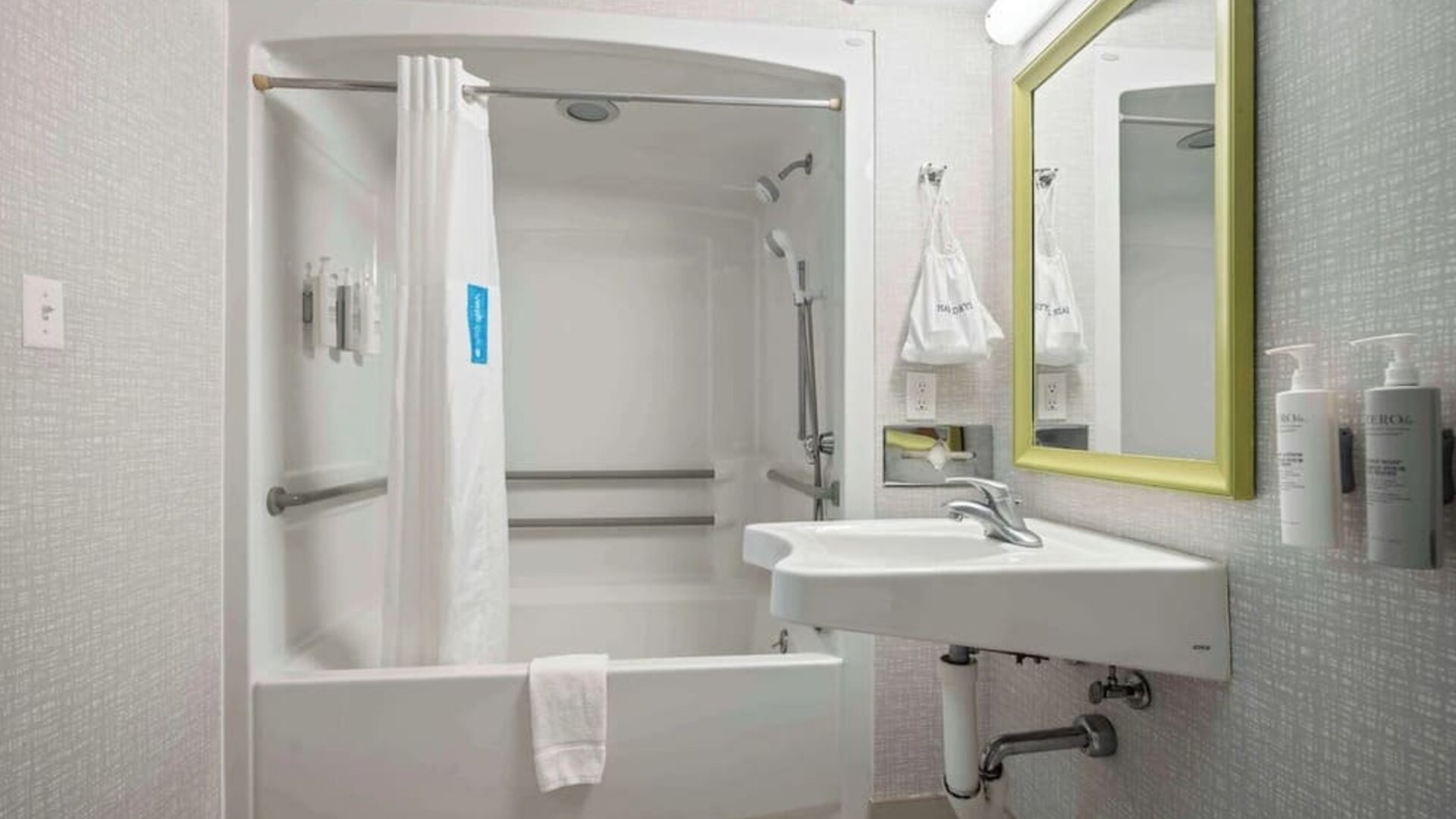 Accessible guest bathroom featuring a roll-in shower, support grab bars and modern vanity at Hampton Inn Ridgefield Park.