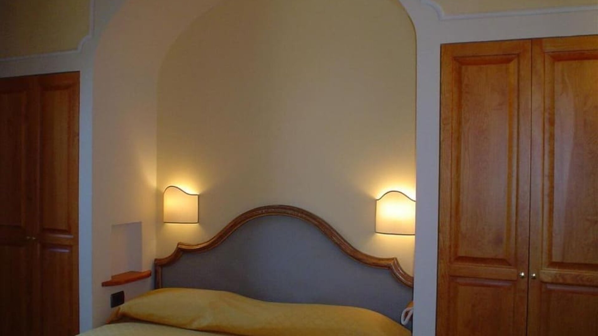 Cozy guest room with a double bed, upholstered headboard, built-in wardrobe, and warm ambient lighting.