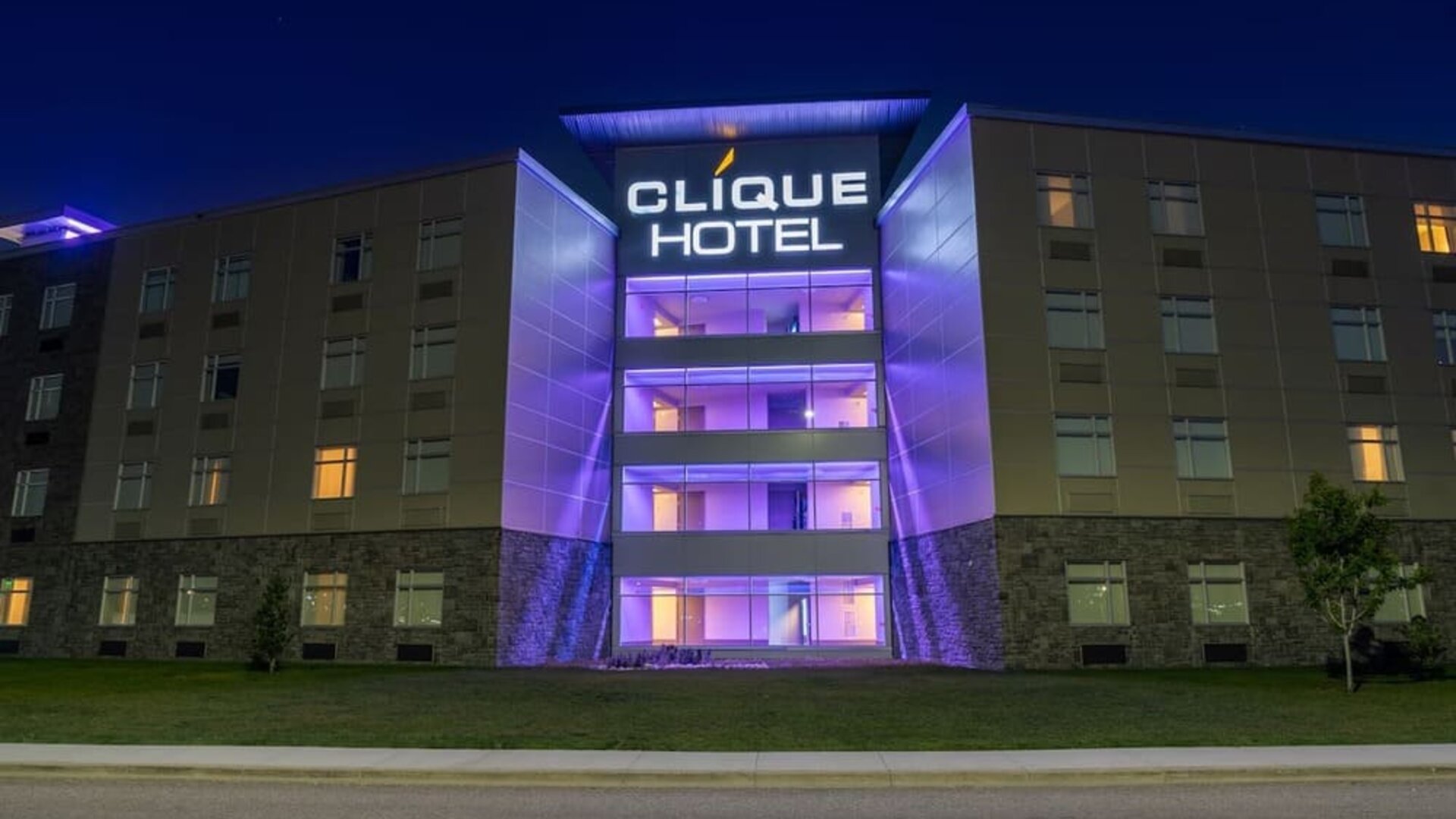 Hotel exterior at night with illuminated Clique Hotel signage and purple accent lighting on the central entrance. Hotel Clique Calgary Airport.
