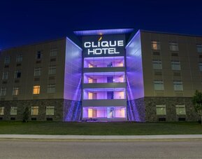 Hotel exterior at night with illuminated Clique Hotel signage and purple accent lighting on the central entrance. Hotel Clique Calgary Airport.