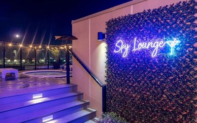 Rooftop Sky Lounge entrance with neon sign, illuminated steps, and hot tub area visible at night. Hotel Clique Calgary Airport.