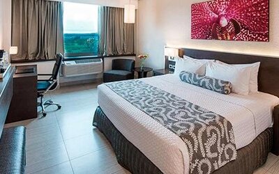 Contemporary king guest room with a large bed, dedicated workspace, flat-screen television, and large windows providing natural light at Crowne Plaza Panama Airport.