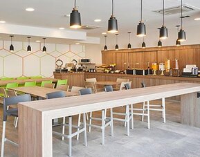 Contemporary breakfast and dining area with communal tables, buffet service, and ample seating for guests.