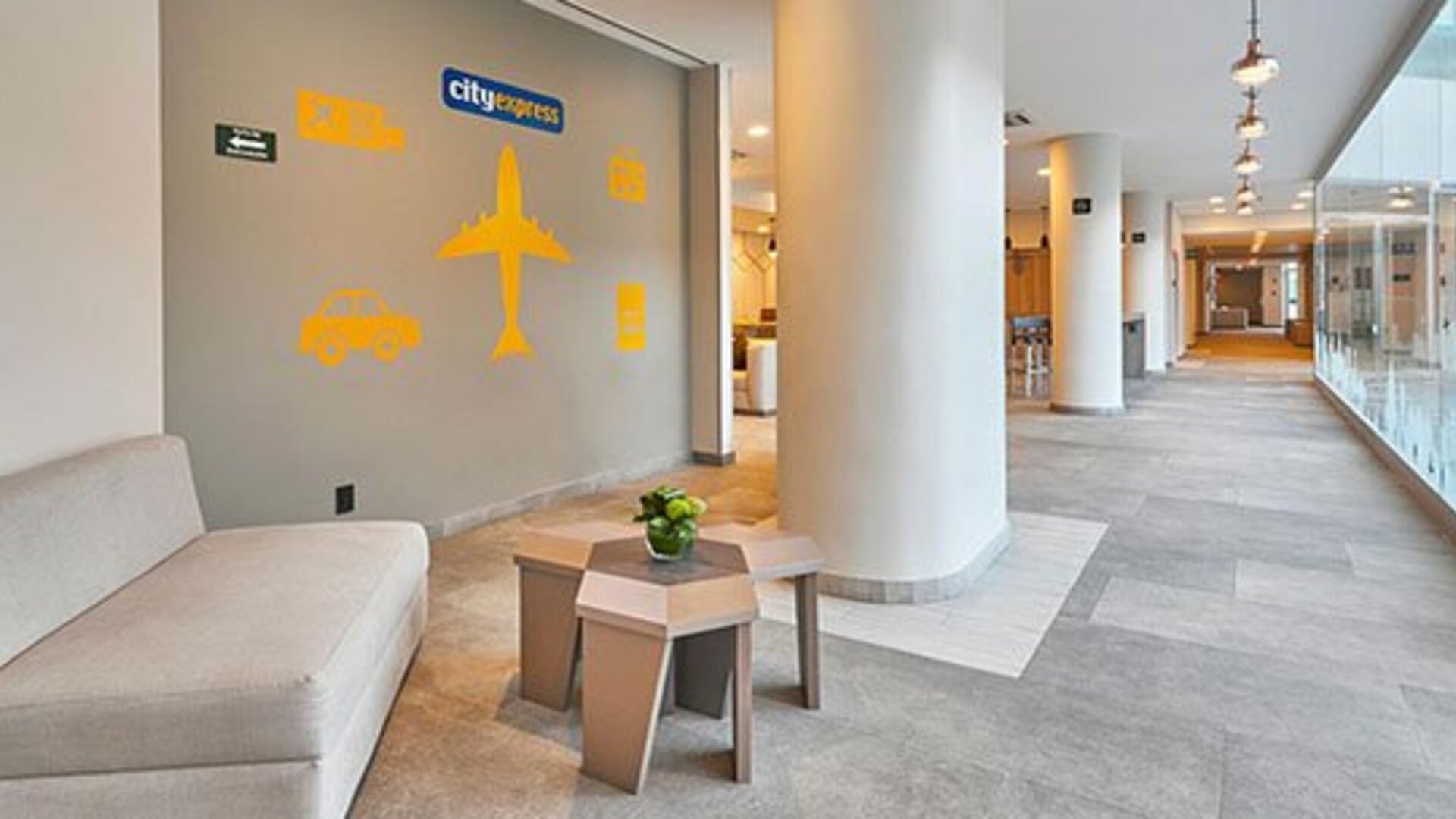 Hallway seating area near reception featuring modern décor and travel-themed accents within City Express by Marriott Aeropuerto Ciudad de México.