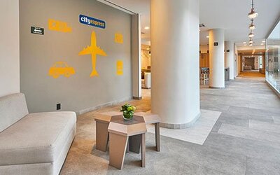 Hallway seating area near reception featuring modern décor and travel-themed accents within City Express by Marriott Aeropuerto Ciudad de México.