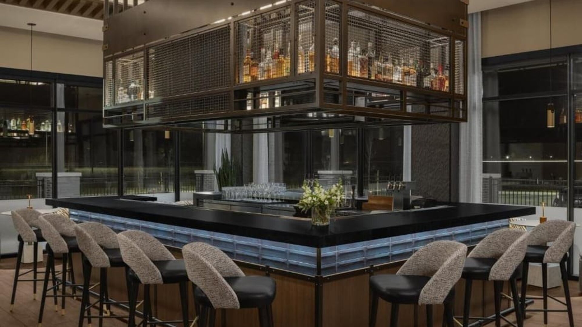 Contemporary hotel bar with wraparound seating, suspended liquor display, and elegant lighting at Hyatt Place Bozeman Yellowstone Airport.