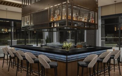 Contemporary hotel bar with wraparound seating, suspended liquor display, and elegant lighting at Hyatt Place Bozeman Yellowstone Airport.