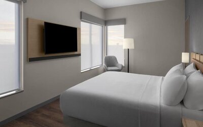 King guest room with large windows, wall-mounted television, lounge chair, and contemporary furnishings at Hyatt Place Bozeman Yellowstone Airport.