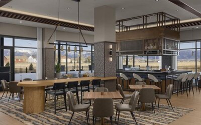 Modern dining area with communal tables, stylish bar seating, and floor-to-ceiling windows at Hyatt Place Bozeman Yellowstone Airport.