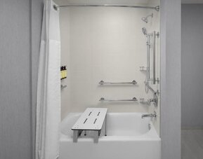 Accessible bathroom with bathtub, grab bars, handheld showerhead, and transfer bench at Hyatt Place Bozeman Yellowstone Airport.