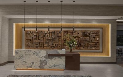 Reception desk with marble front, wood accent wall, and contemporary lighting at Hyatt Place Bozeman Yellowstone Airport.