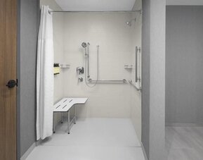 Accessible roll-in shower with grab bars, handheld showerhead, and built-in transfer bench at Hyatt Place Bozeman Yellowstone Airport.
