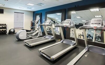 Fitness center with treadmills, cardio machines, free weights, and mirrored wall at Hampton Inn & Suites Orlando at SeaWorld.
