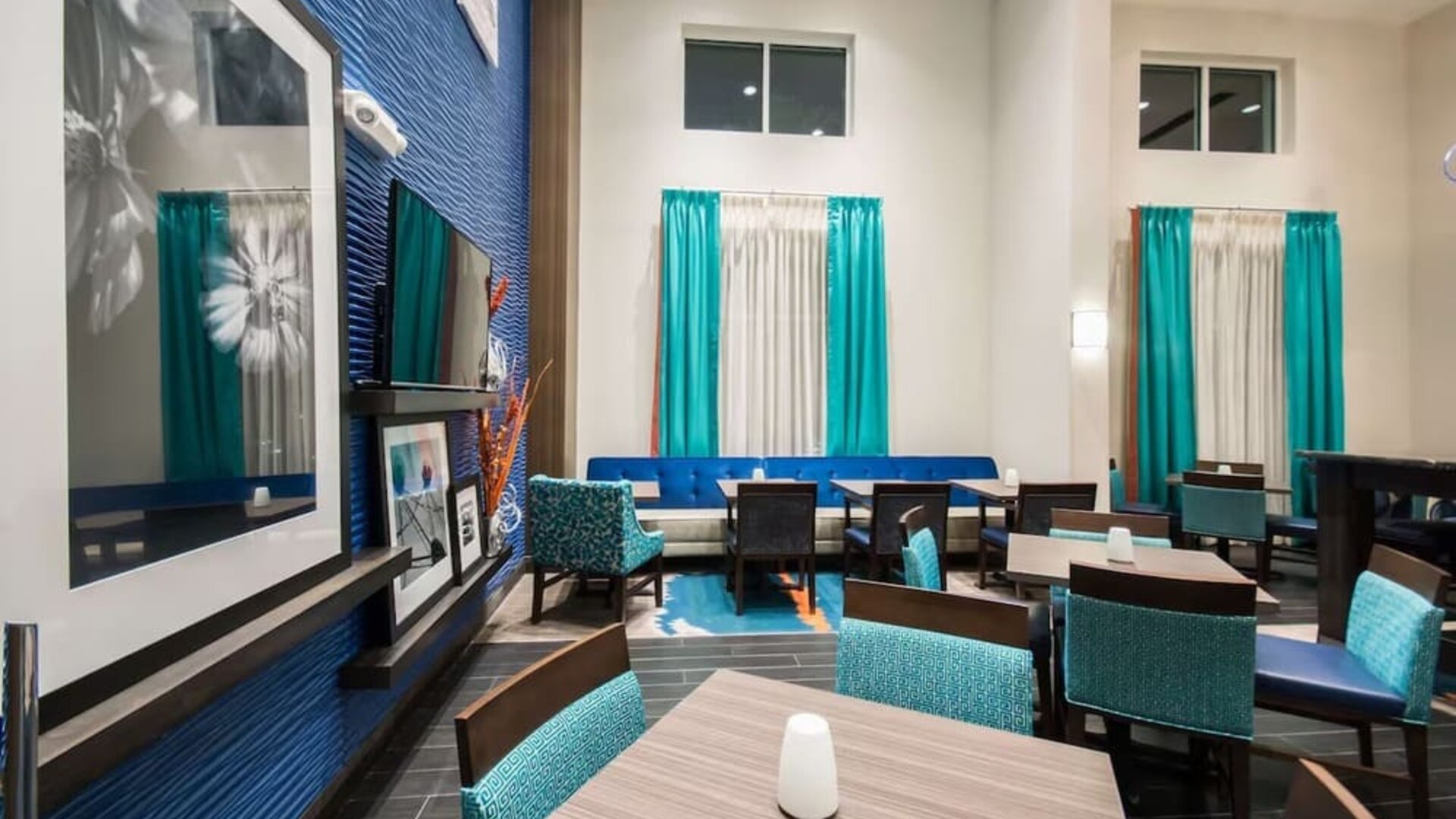 Lobby lounge with dining tables, seating area, and high ceilings at Hampton Inn & Suites Orlando at SeaWorld.