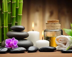 Spa-inspired arrangement with bamboo, smooth stones, candles, orchid flower, essential oil, and rolled towel.
