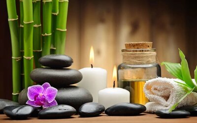 Spa-inspired arrangement with bamboo, smooth stones, candles, orchid flower, essential oil, and rolled towel.