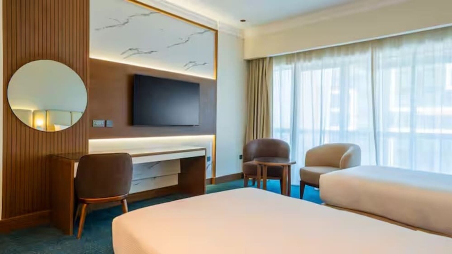 Contemporary guest room with two twin beds, large window, seating area, wall-mounted television, and workspace.