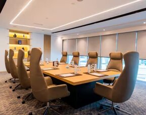 Professional boardroom with executive chairs, large conference table, floor-to-ceiling windows, and modern lighting.
