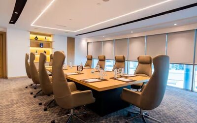 Professional boardroom with executive chairs, large conference table, floor-to-ceiling windows, and modern lighting.